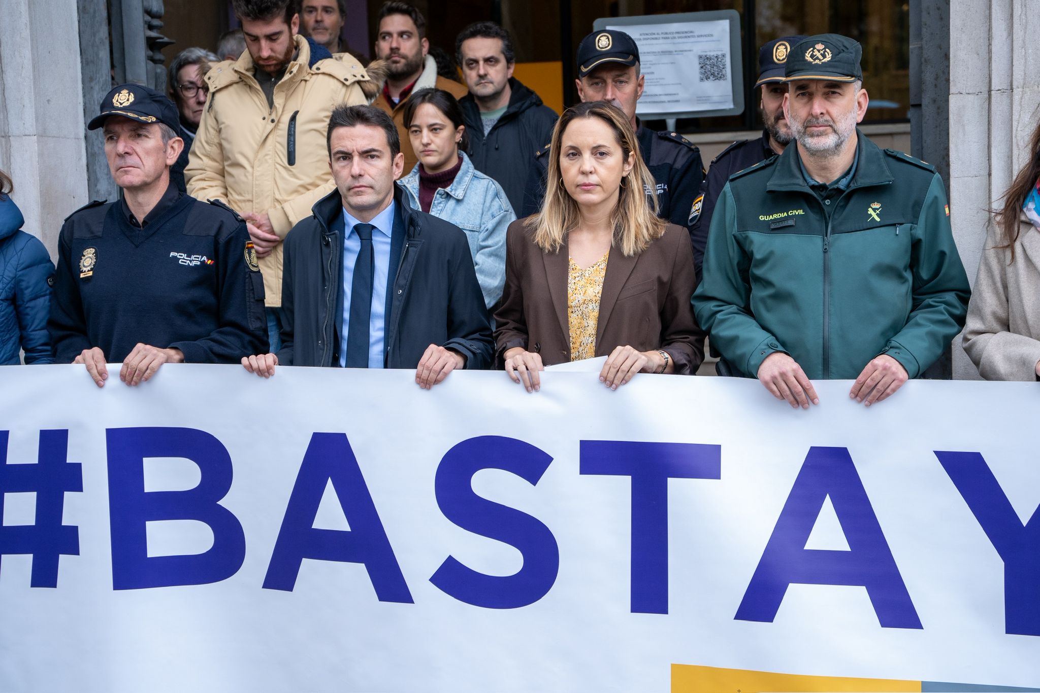 El delegado del gobierno junto con otras autoridades manteniendo la pancarta #BASTA YA